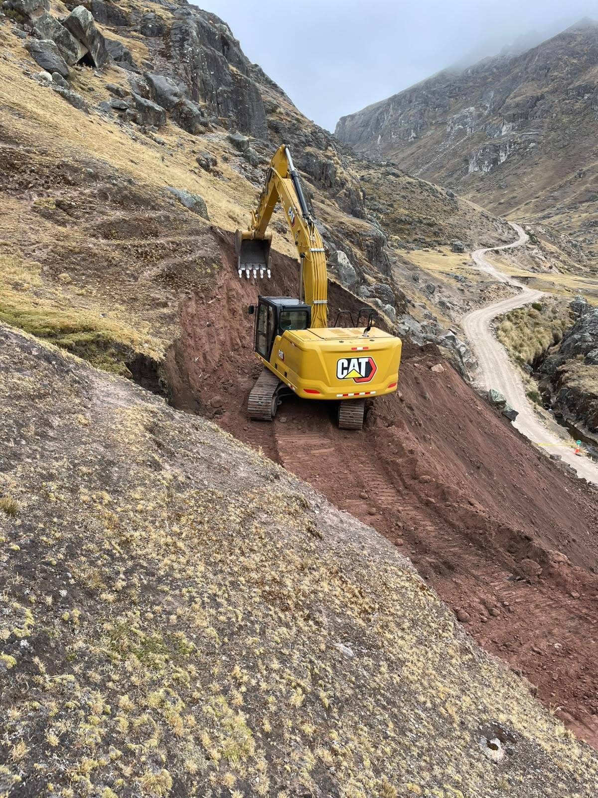 Excavadora CAT abriendo camino en talud de montaña